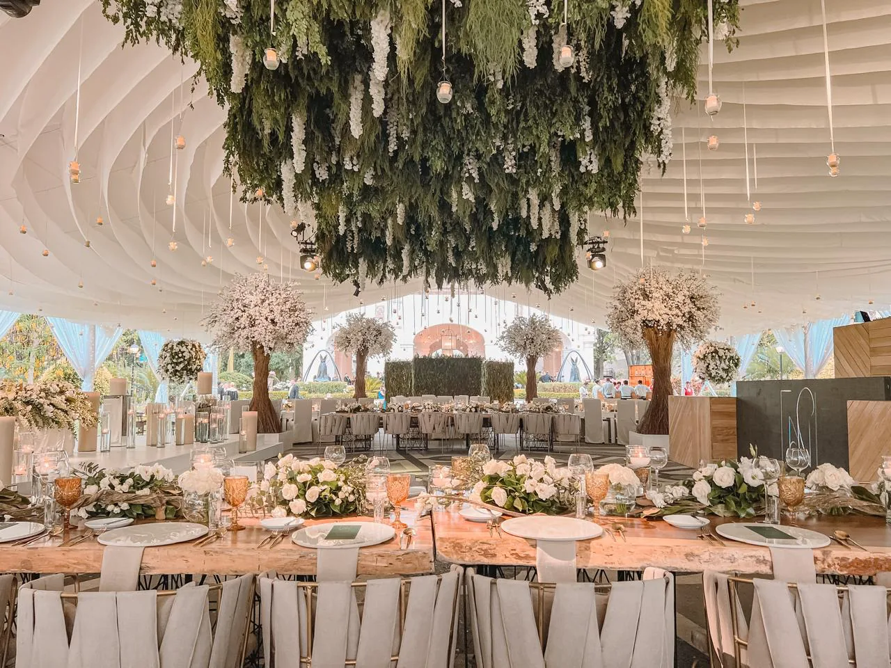 Recepción en carpa de hacienda con techo floral suspendido y mesas elegantes