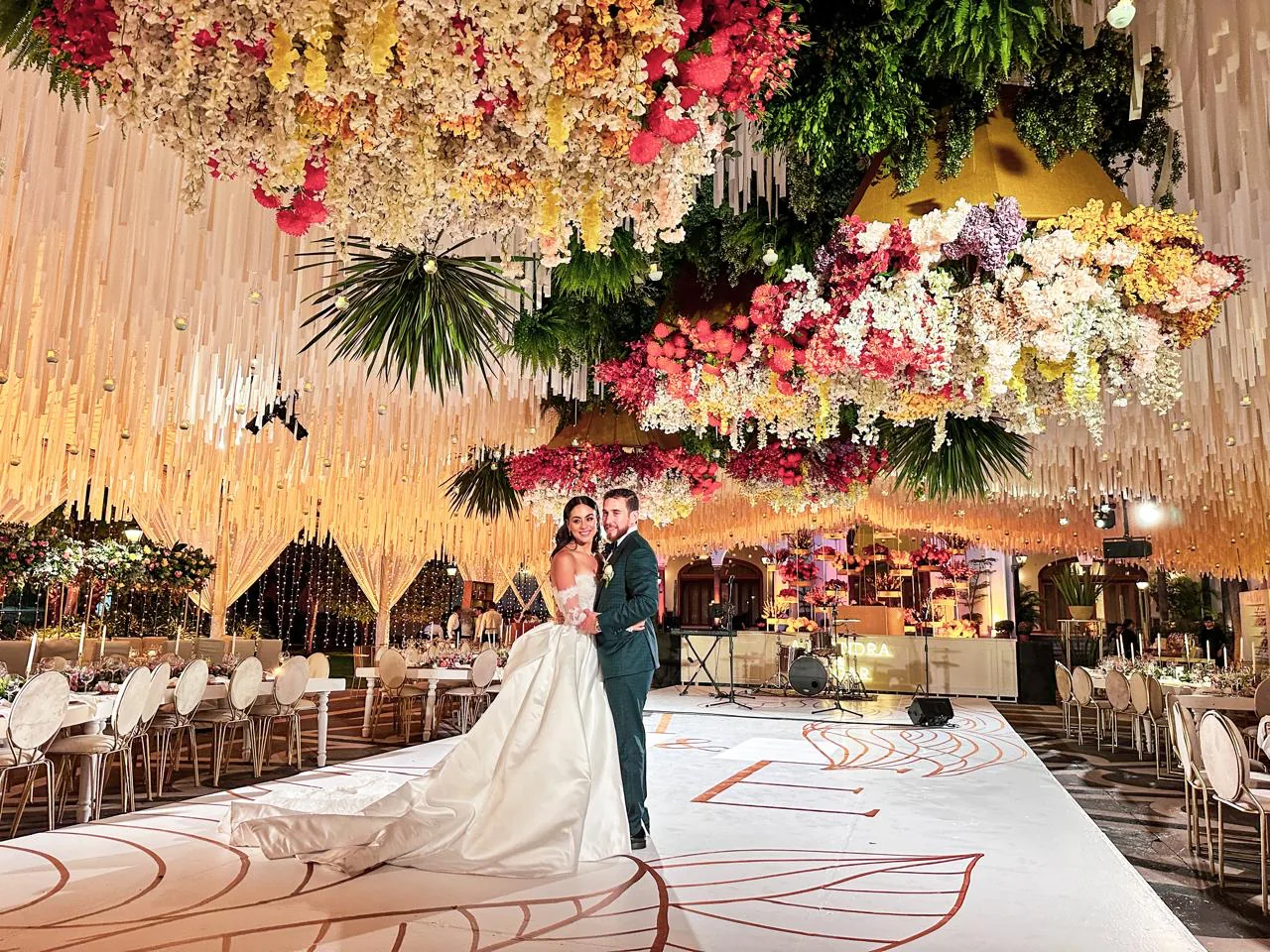 Pareja en recepción de hacienda con techo floral colorido y piso decorativo
