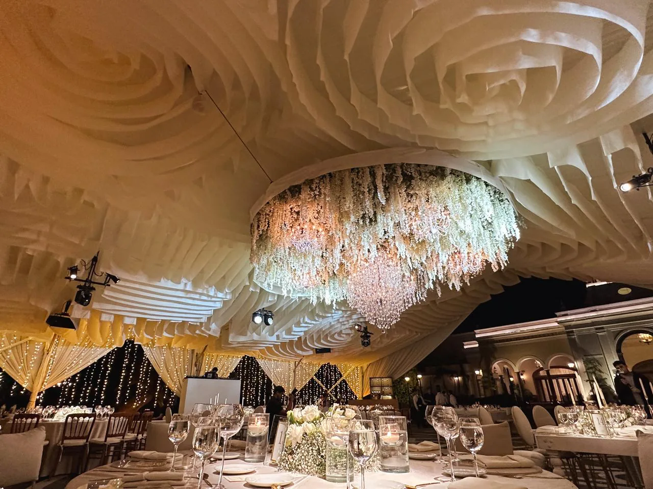 Recepción en salón con techo entelado ondulado dorado, candelabros de cristal colgantes y luces cálidas