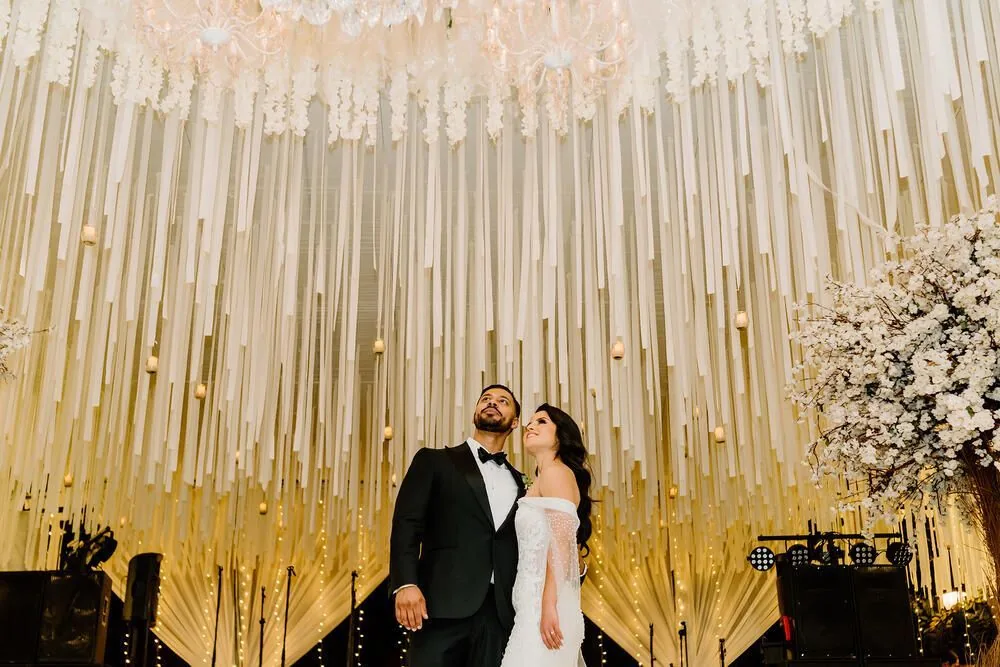 Recepción de boda en salón con techos entelados, candelabros y mesas con velas